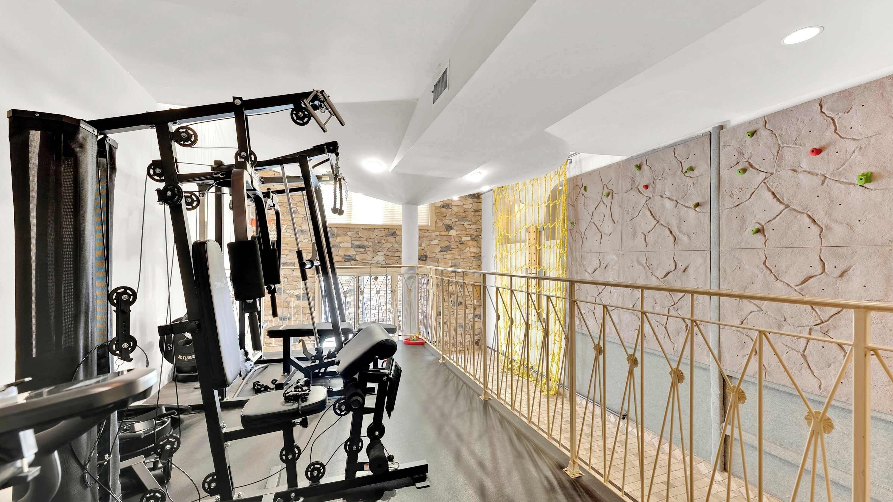 Une salle de sport équipée de matériel d’exercice, un mur en pierre avec des prises d’escalade et une barrière faite d’une corde jaune.