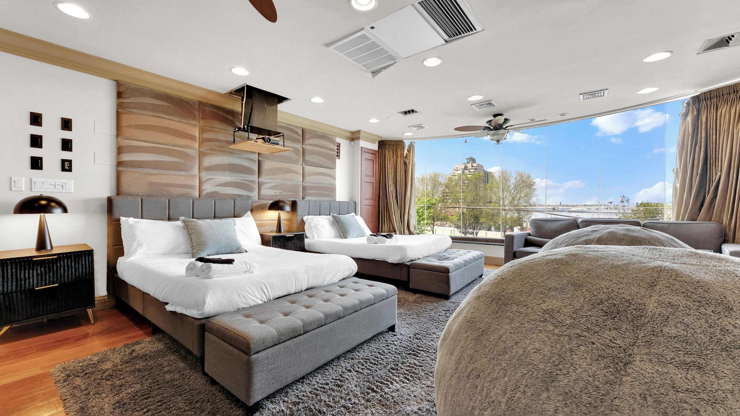 A modern hotel room with a large bed, a sofa, a chair, and a view of the city.