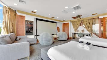 Quarto de hotel com uma cama grande, um sofá, duas áreas de estar redondas, uma escrivaninha e um ventilador de teto.