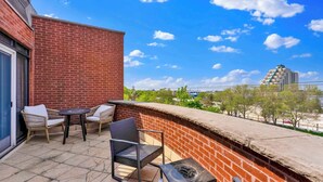 A balcony with a brick wall, a table, two chairs, and a view of a cityscape. - Prime 5BR Home Retreat | Sleeps 16 | South St Pier (Philadelphia)