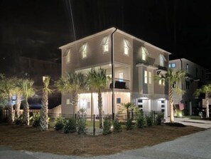 A multi-story building with a balcony, surrounded by a fence and palm trees.