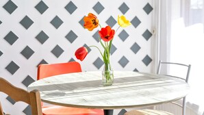 Une table ronde sur laquelle est posé un vase en verre transparent contenant des tulipes, le tout placé devant un mur orné d’un motif géométrique.