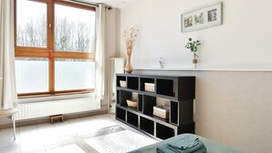 Une chambre à coucher comprenant un lit, une table de chevet, un radiateur, une fenêtre et une étagère avec des objets décoratifs.