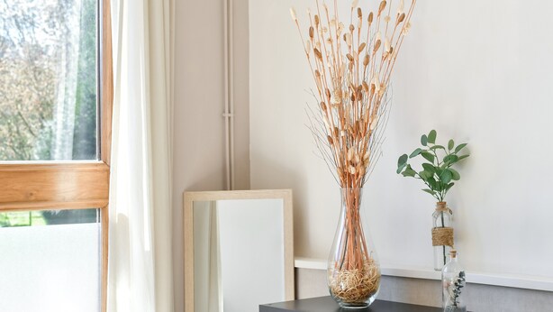 Une pièce avec une fenêtre, une console en bois foncé et deux vases en verre contenant des plantes séchées.