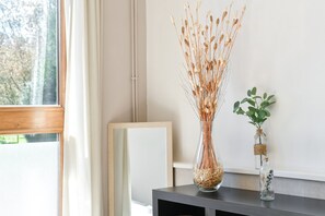 Una habitación con ventana, una consola de madera oscura y dos floreros de vidrio con plantas secas.