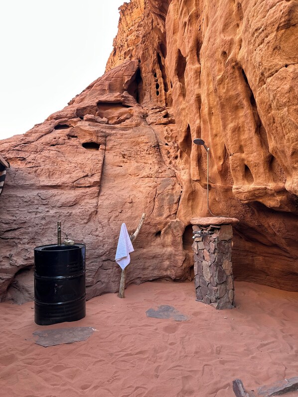 Un barril negro, una toalla y una estructura de piedra frente a un muro de roca roja.