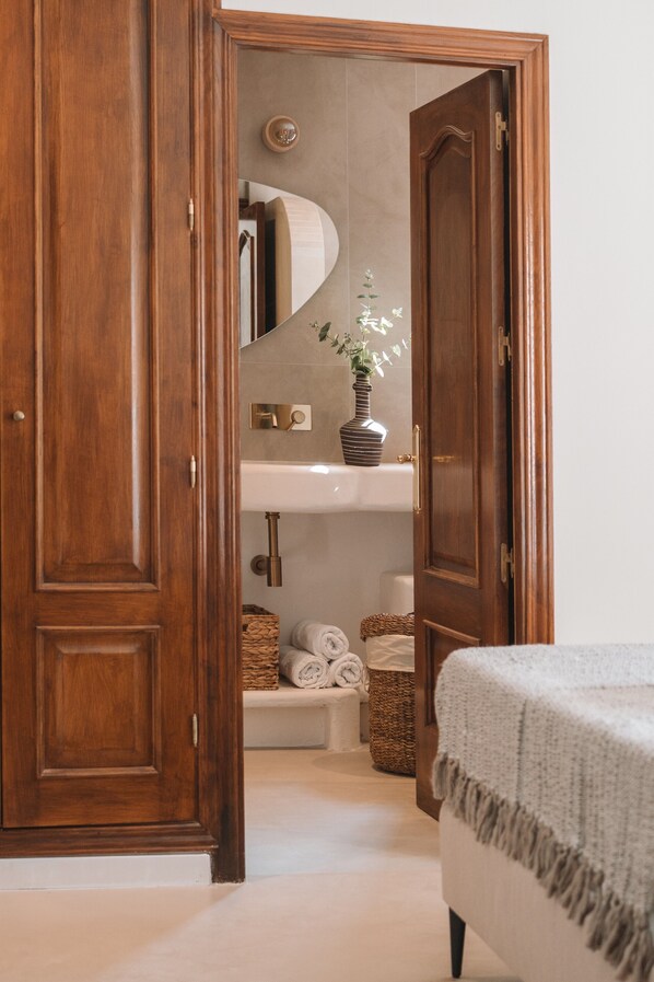 Un armario de madera, un lavabo blanco y una cama con una colcha blanca.