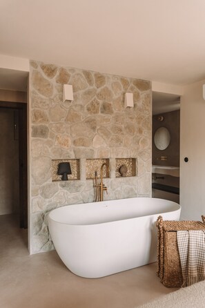 Ein modernes Badezimmer mit Steinwand, einer freistehenden Badewanne, einem Spiegel und einem Handtuchhalter.