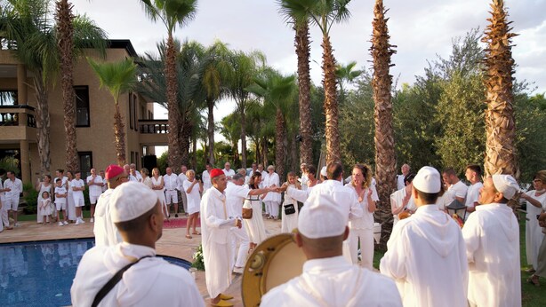 A group of people in white robes gathered around a pool area with palm trees and a building in the background. - Villa Marrakech-Luxe, Spa, Unforgettable Weddings & Parties (Marrakech)