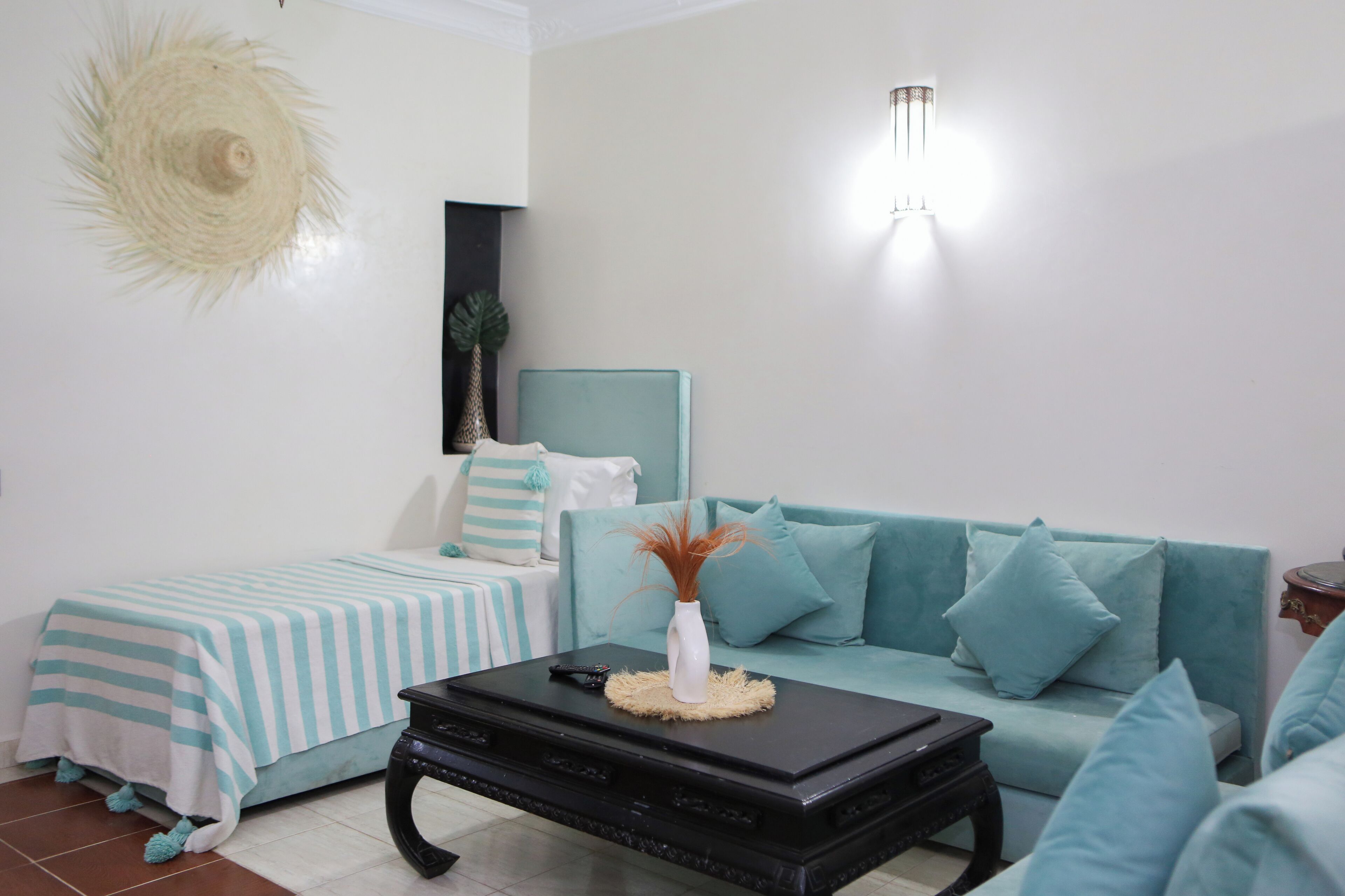 A modern living room with a teal sofa, a striped bed, and a black coffee table with a vase.