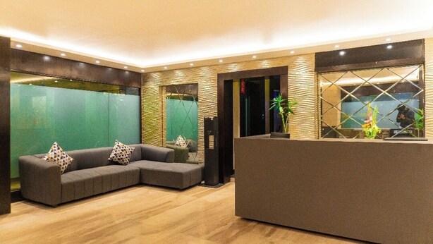 Un espace d’accueil moderne comprenant un comptoir de réception, un canapé d’angle agrémenté de coussins à motifs et un grand miroir qui reflète l’intérieur.