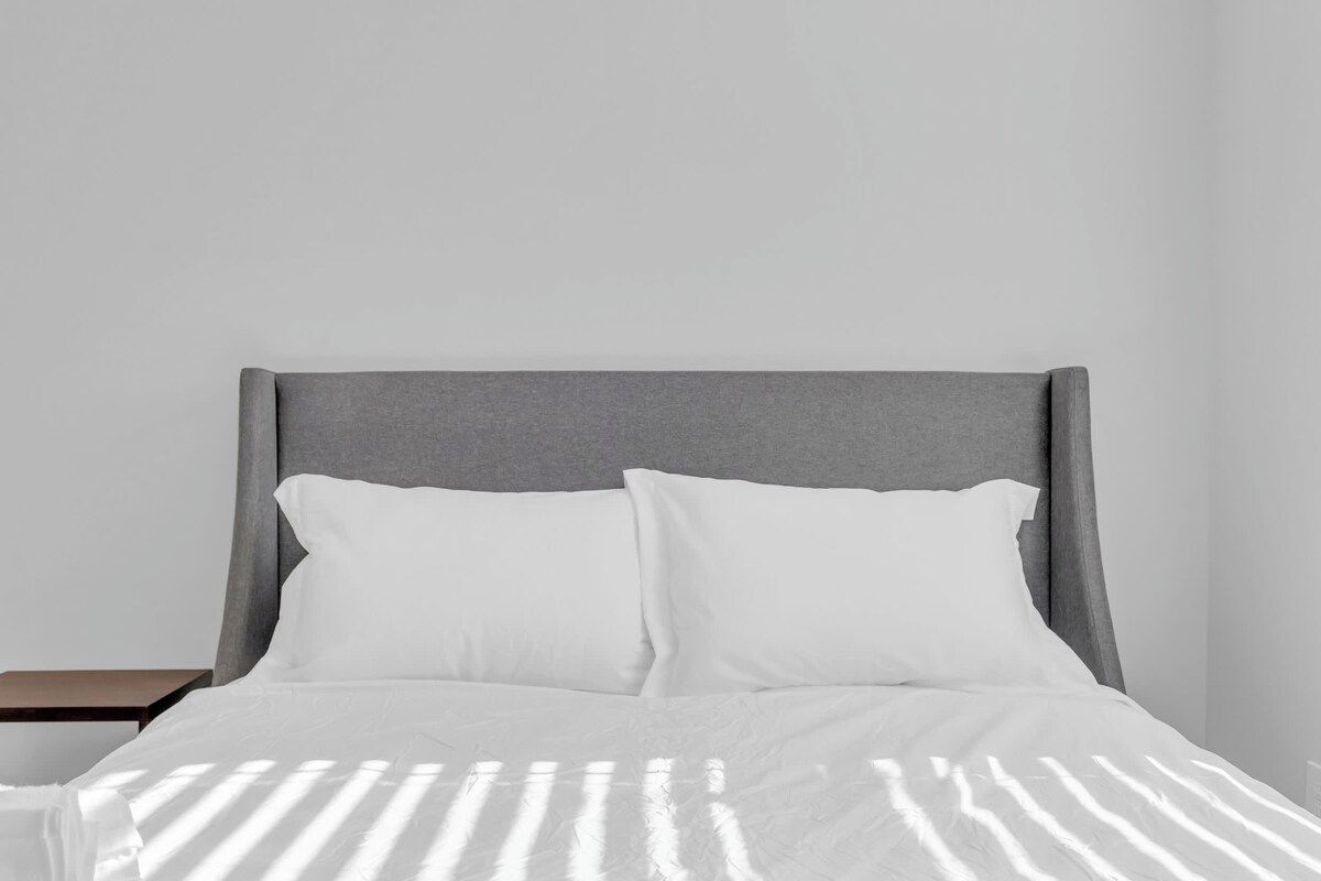 A bed with a grey headboard, white bedding, and a nightstand.