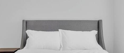 A bed with a grey headboard, white bedding, and a nightstand.