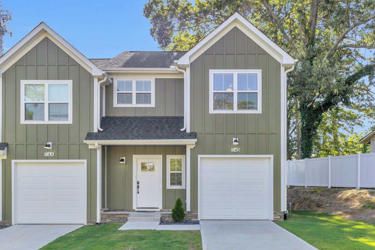 Une maison à deux étages avec un porche à l’avant, deux portes de garage et un petit jardin devant.