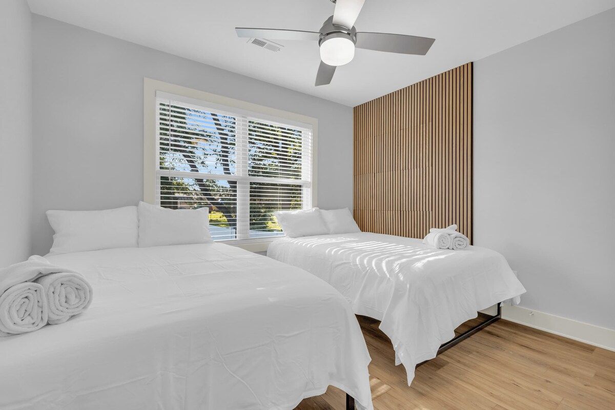 Ein Hotelzimmer mit zwei Betten, einem Deckenventilator und einem großen Fenster mit Jalousien.