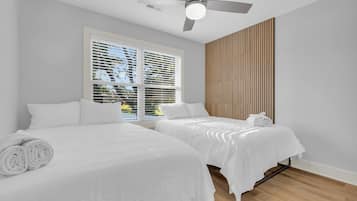 Ein Hotelzimmer mit zwei Betten, einem Deckenventilator und einem großen Fenster mit Jalousien.