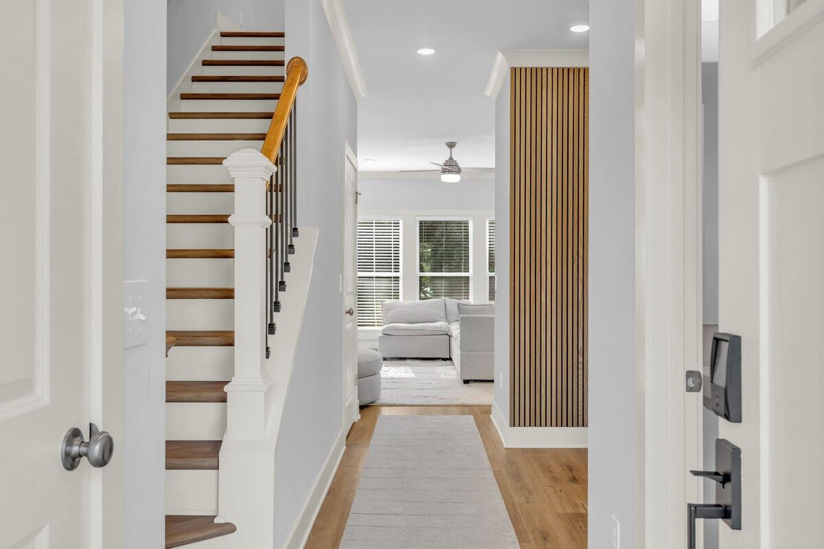A hallway with a wooden staircase, a white door, and a grey rug leading to a living area with a grey sofa.