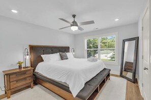 Un dormitorio con cama, mesita de noche, banco, ventilador de techo y ventana con persianas.