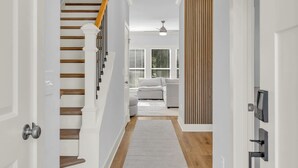 A modern interior with a staircase, a living area with a sofa, and a wooden accent wall. - Modern Stay | Luxe 3BR | Sleeps 10 | 2 Min DT (Spartanburg)