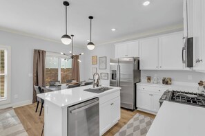 Una cocina moderna con armarios blancos, electrodomésticos de acero inoxidable e iluminación colgante.