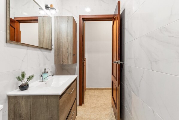 A bathroom with a wooden vanity, a mirror, a sink, and a door leading to another room.