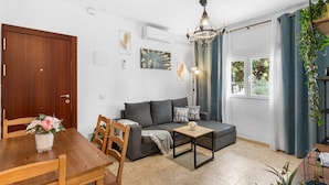 Ein Wohnzimmer mit einer Couch, einem Esstisch mit Stühlen, einer Chandelier und Blick ins Freie.
