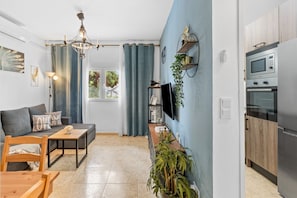 A modern living room with a sofa, a dining table, a chandelier, a TV mounted on the wall, and a kitchen with an oven and microwave. - Apartment 'Centro De Marbella' with Wi-Fi and Air Conditioning (Marbella)