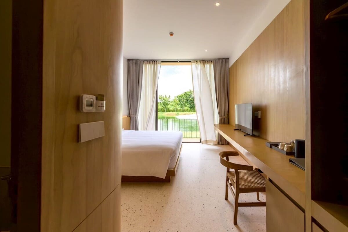 A hotel room with a bed, a desk with a TV, a chair, and a balcony with curtains.