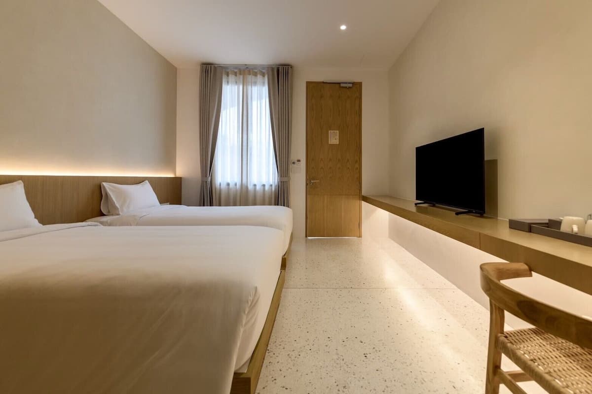 A hotel room with two beds, a TV, and a wooden desk.