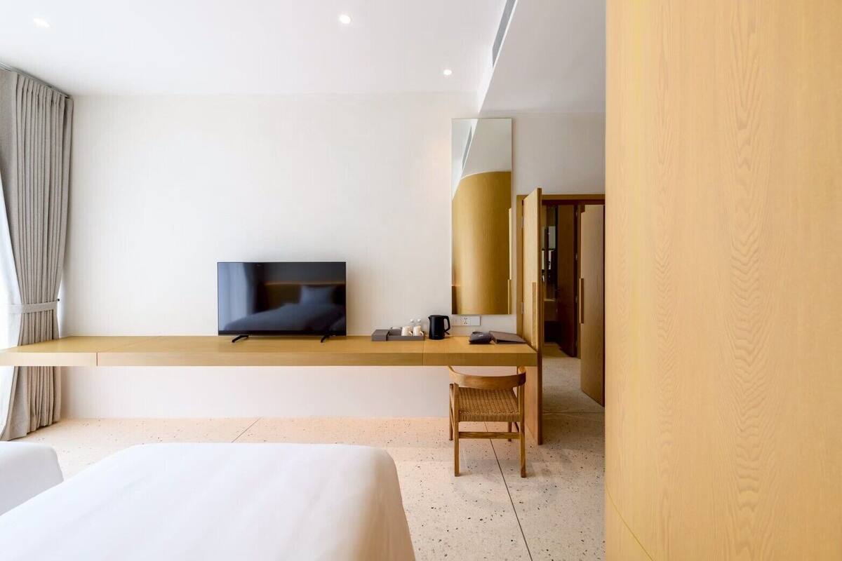 A modern hotel room with a large bed, a desk with a chair, a television, and a wardrobe.
