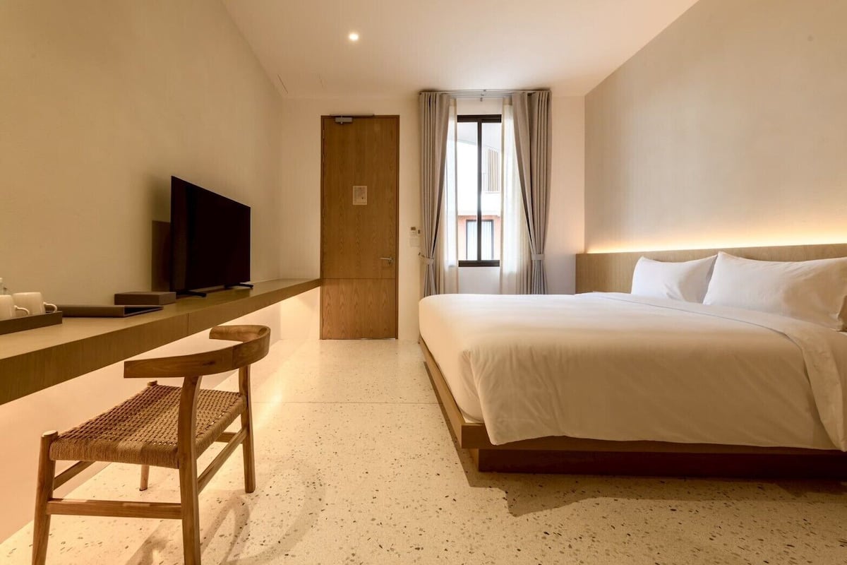 A hotel room with a bed, a TV, a desk with a chair, and a door leading to a balcony.