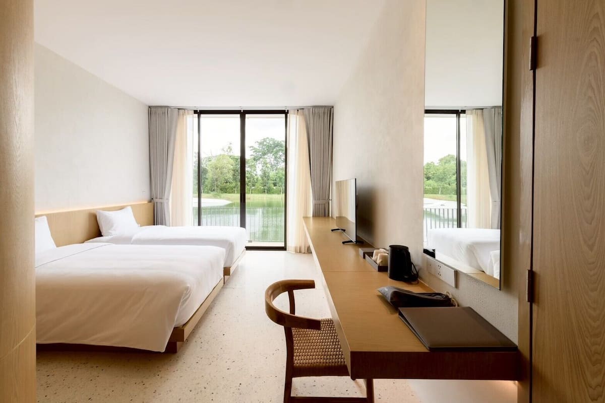 A hotel room with two beds, a desk with a laptop, a TV, and a view of a lake.