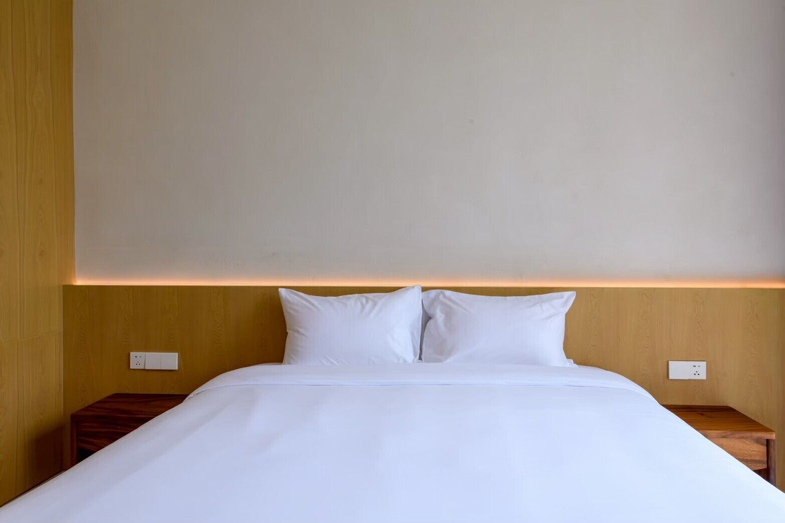 Un lit bien fait, avec du linge de lit blanc, dans une pièce aux murs recouverts de lambris en bois et au design simple et épuré.