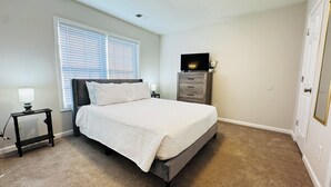 Ein Schlafzimmer mit Bett, Nachttisch, Kommode und Fernseher.