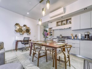 A modern kitchen with white cabinets, a dining area with a wooden table and chairs, and a decorative hexagonal wall piece.
