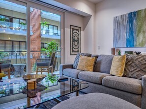 Un salón moderno con una mesa de centro de vidrio, un sofá con cojines estampados y vistas a un balcón con muebles de exterior.