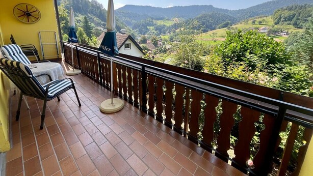 Een balkon met uitzicht over een vallei, een stoel en een tafel.