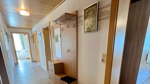 Een gang met een houten bankje, een kapstok en een lijst met een afbeelding aan de muur.