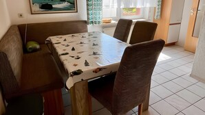 Een eethoek met een tafel, stoelen, een bank, een prullenbak en een schilderij aan de muur.