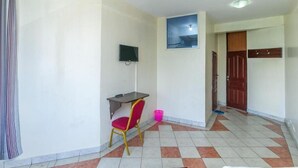 Un pasillo con suelo de baldosas, un escritorio con una silla, un televisor montado en la pared y una puerta.