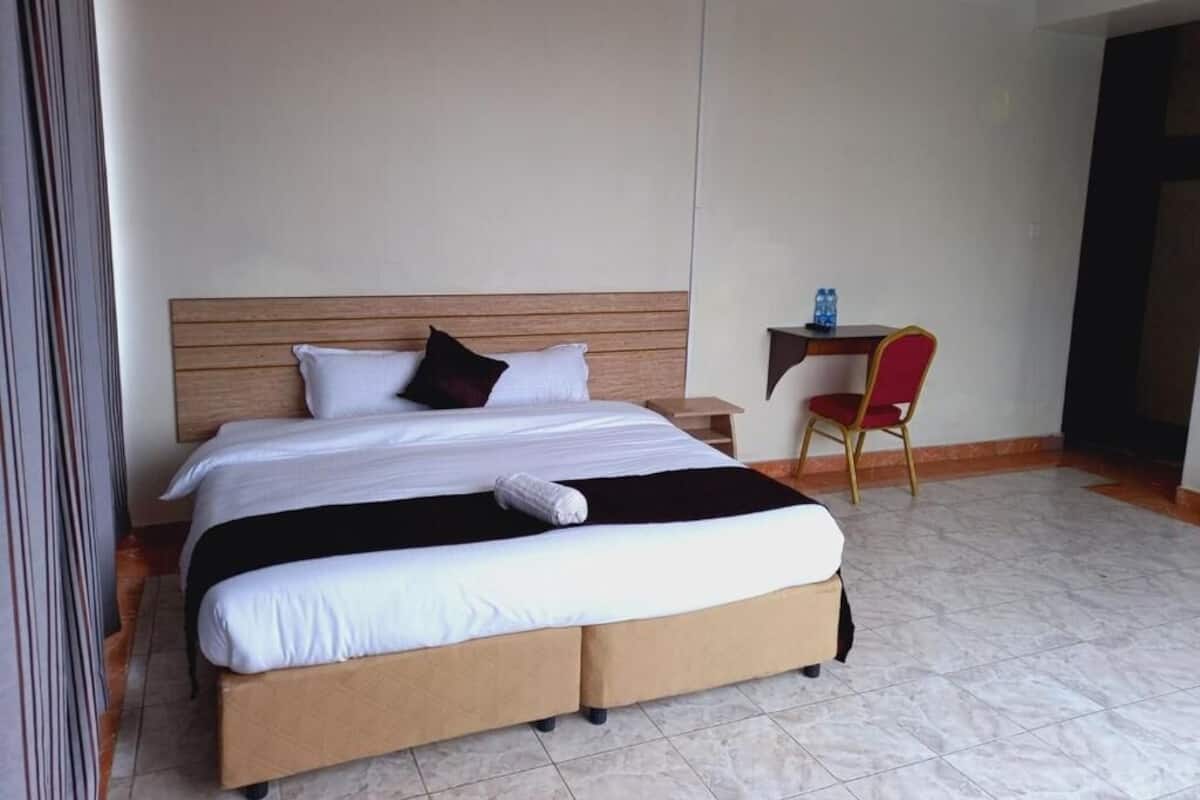 A hotel room with a large bed, a bedside table with a water bottle, and a red chair.