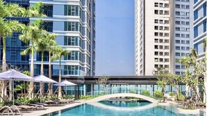A swimming pool with lounge chairs and umbrellas, surrounded by tall buildings and palm trees. - Skyway White & Silver Riverside Resident - Binh Thanh, HCM (Ho Chi Minh City)