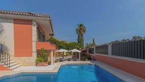 Ein Schwimmbecken mit einer gefliesten Umrandung, einer Treppe und Sitzgelegenheiten mit Sonnenschirmen.