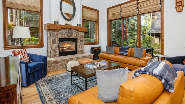 A cozy living room with a stone fireplace, leather sofas, a coffee table, and large windows with blinds.
