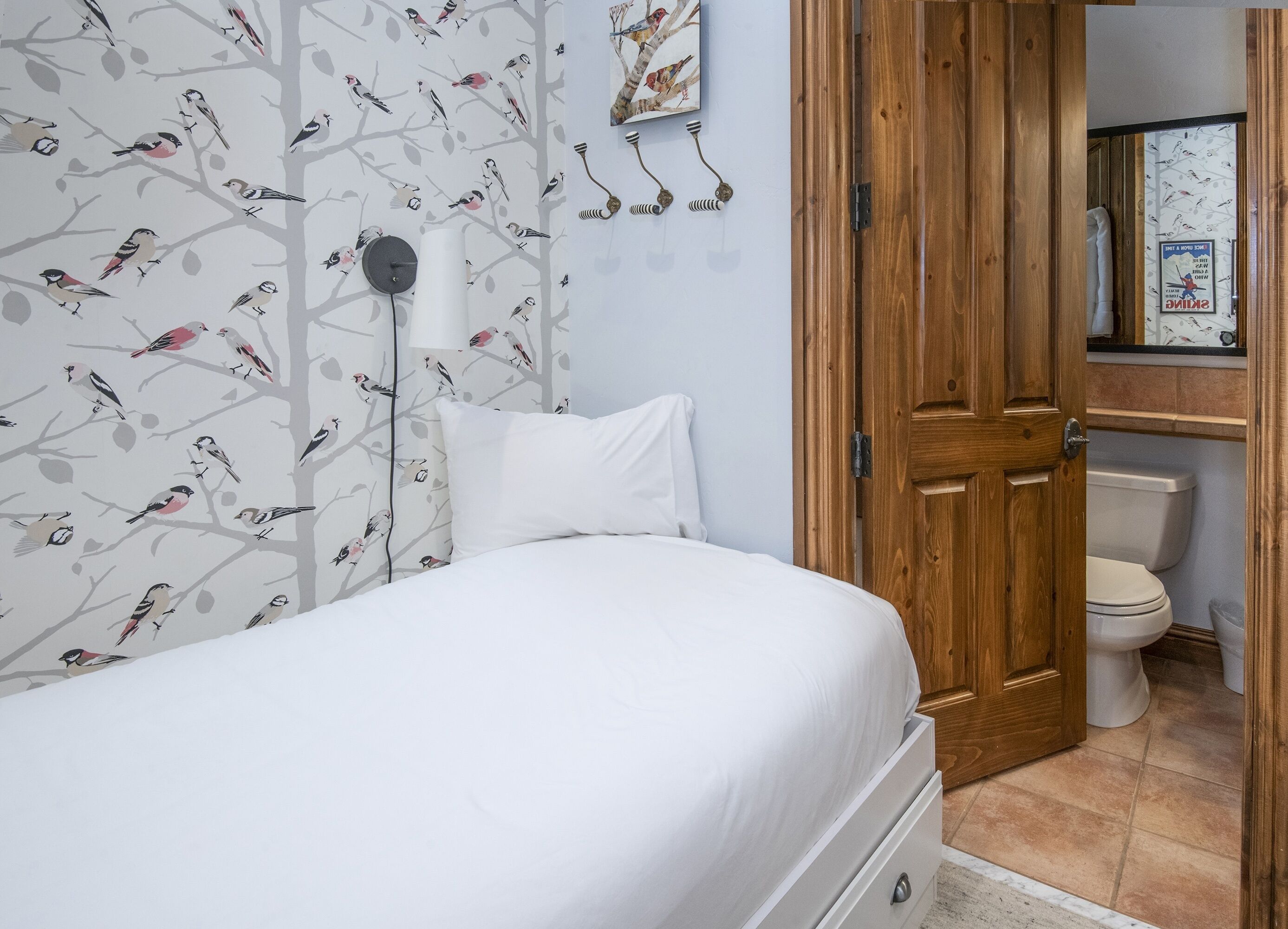 Quarto com uma cama, uma porta de madeira e um toalete visível através de uma porta aberta.
