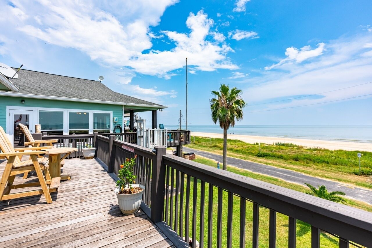 A wooden deck with outdoor seating, a view of the beach, and a house with large windows.