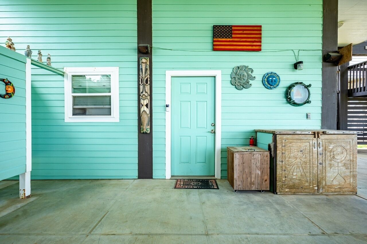 A teal house exterior with a white door, a small window, and a wooden cabinet with drawings.