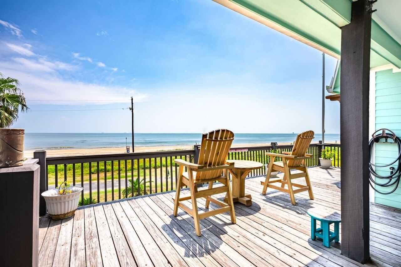 A wooden deck with two Adirondack chairs facing a beach.