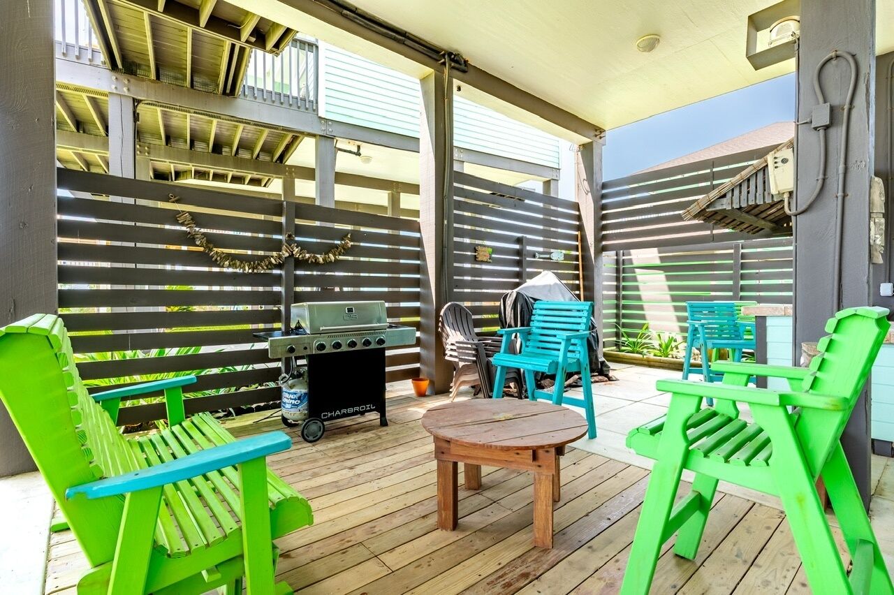 An outdoor patio with a grill, green chairs, and a table.