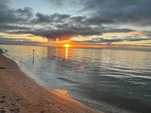 A beach with a sunset over the water, a flagpole, and a sandy shore. - Coastal Cove Suite with balcony - close to hot springs. (Fingal)